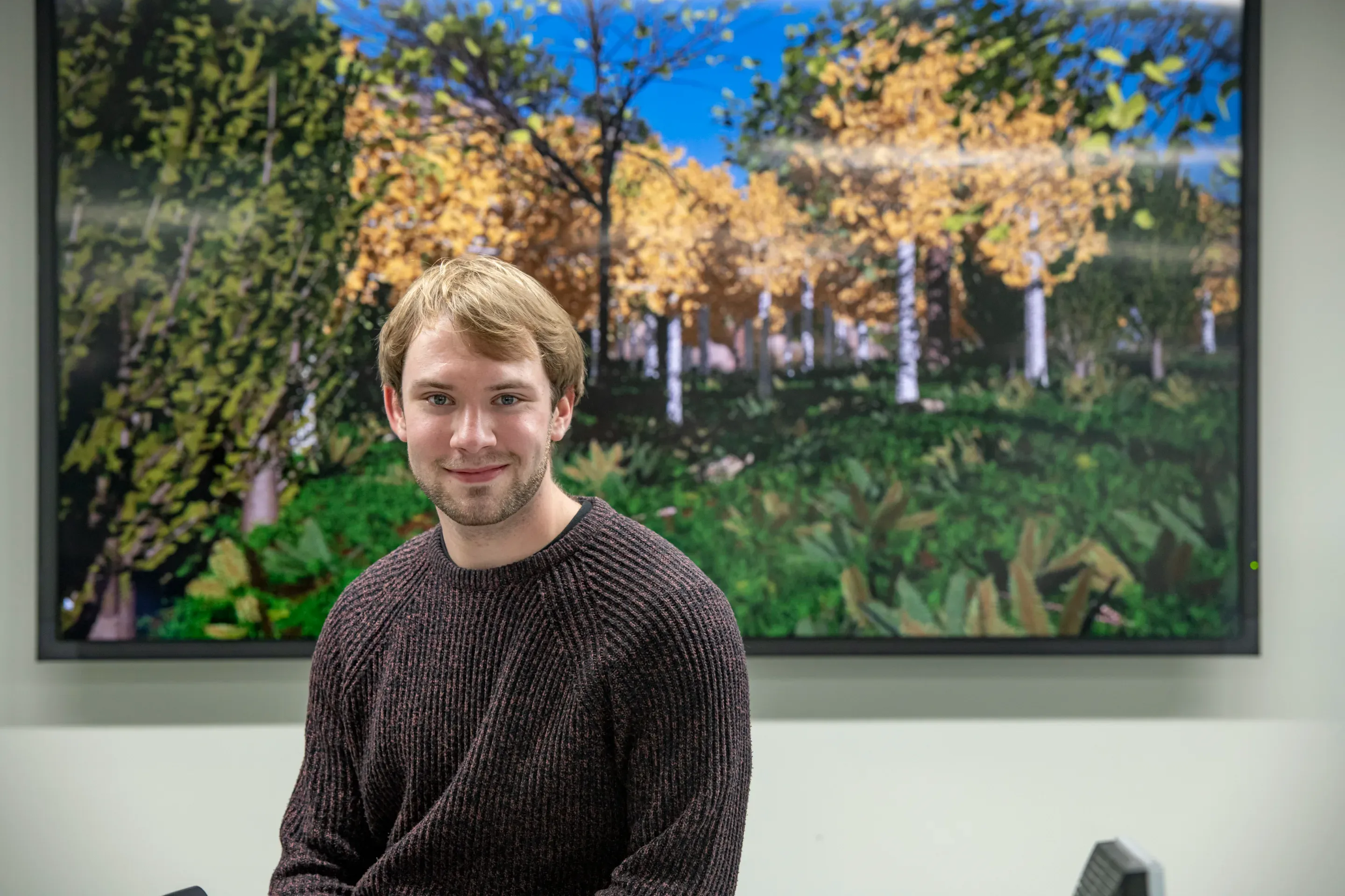 Photo of Callum Newlands sitting in front of a screen with a virtual forest scene on it.